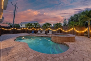 A backyard with a swimming pool, a hot tub, and a wooden fence decorated with string lights.