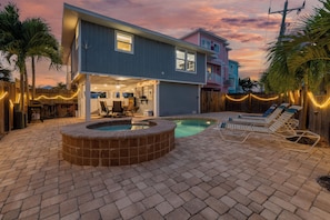 A two-story house with a backyard featuring a swimming pool, lounge chairs, and a patio area.