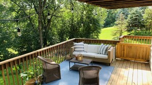 Eine Holzterrasse mit einer Korbuschette, zwei Korbstühlen und einem kleinen Tisch.
