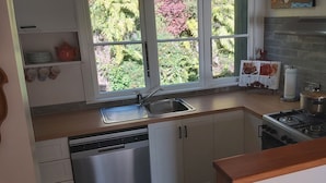 A kitchen with a sink, stove, and a window overlooking greenery.