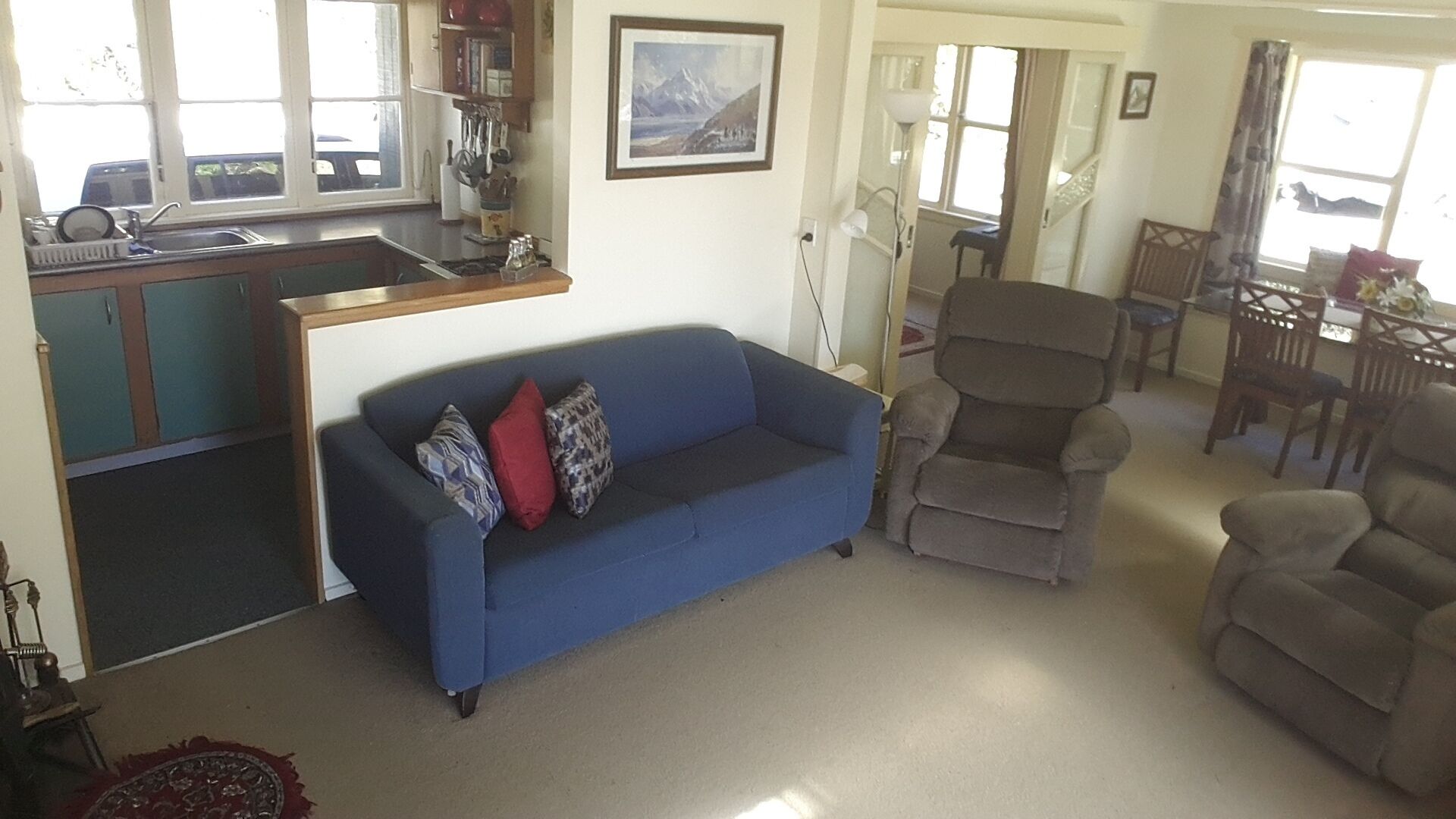 Una sala de estar con un sofá azul, un sillón marrón y un comedor con mesa y sillas.
