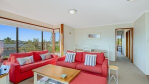 Ein modernes Wohnzimmer mit roten Sofas, einem Holztisch und großen Fenstern mit Blick ins Freie.