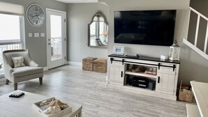 A living room with a flat-screen TV, a comfortable armchair, a coffee table, and a bookshelf.