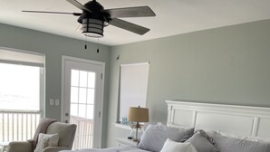 A bedroom with a bed, a chair, a ceiling fan, and a window.