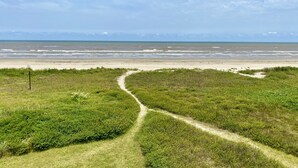 A coastal path leading to a beach with a clear view of the ocean and distant mountains.