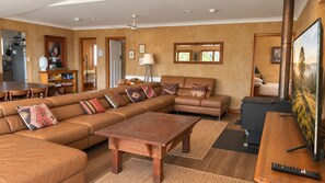 A spacious living room with a large sectional sofa, a wooden coffee table, and a television. - The Farmhouse — Relax in a rustic private sanctuary, pet and family friendly (Canyonleigh)