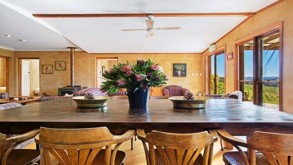 A spacious dining area with a large wooden table, several chairs, and a ceiling fan. - The Farmhouse — Relax in a rustic private sanctuary, pet and family friendly (Canyonleigh)