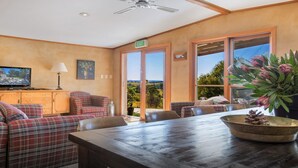 A cozy room with a wooden table, plaid sofas, and a television on a cabinet. - The Farmhouse — Relax in a rustic private sanctuary, pet and family friendly (Canyonleigh)