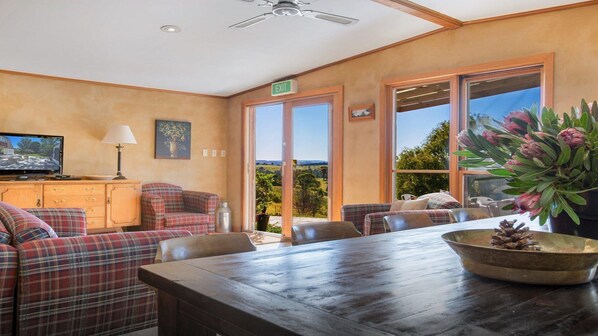 A cozy room with a wooden table, plaid sofas, and a television on a cabinet. - The Farmhouse — Relax in a rustic private sanctuary, pet and family friendly (Canyonleigh)