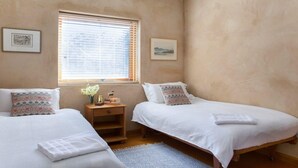 A bedroom with two single beds, a small wooden nightstand, a window with blinds, and a framed picture on the wall. - The Farmhouse — Relax in a rustic private sanctuary, pet and family friendly (Canyonleigh)