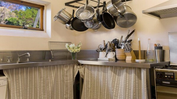 A kitchen with hanging pots, a sink, a stove, and various utensils. - The Farmhouse — Relax in a rustic private sanctuary, pet and family friendly (Canyonleigh)