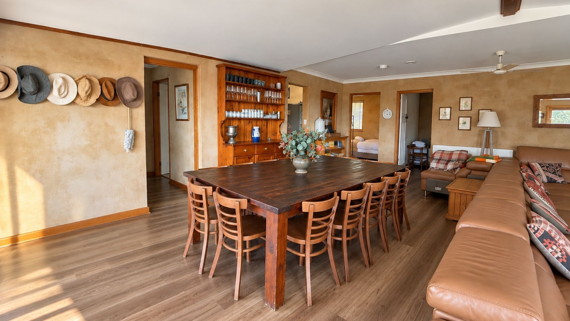 Een ruime woonkamer met een houten eettafel, een leren bank en een verzameling hoeden aan de muur.