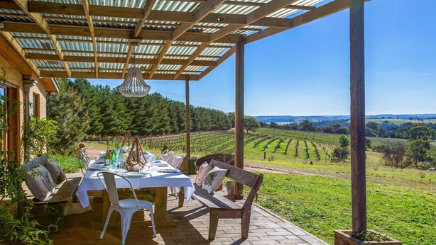 An outdoor dining area with a pergola, a table set for two, and a view of vineyards in the background. - The Farmhouse — Relax in a rustic private sanctuary, pet and family friendly (Canyonleigh)