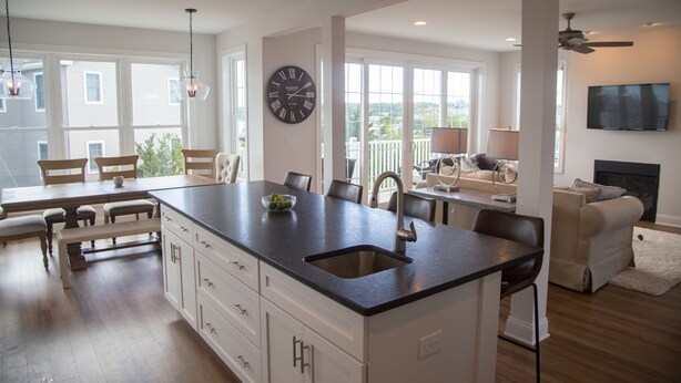 Une cuisine spacieuse avec un grand îlot central, des meubles blancs et une horloge noire au mur.