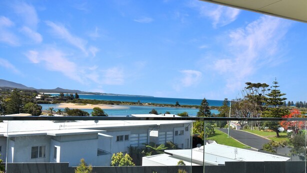 A coastal view from a balcony with a clear sky, a sandy beach, and a calm sea.