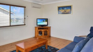 A living room with a wooden entertainment unit, a television, a blue sofa, and a window with blinds.