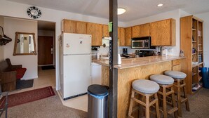 Une cuisine avec des meubles en bois, un réfrigérateur, un four à micro-ondes et un coin bar avec des tabourets.