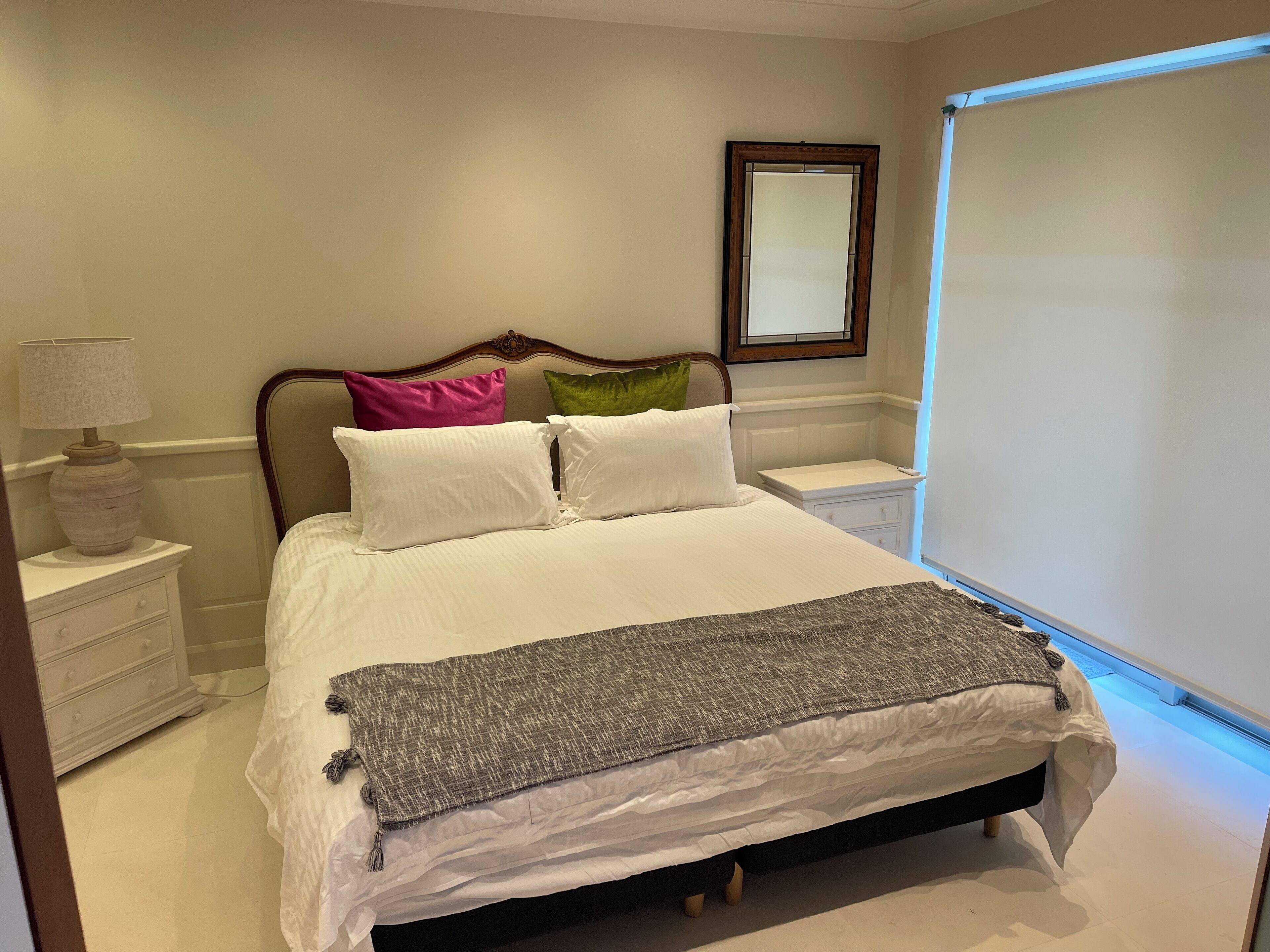 A neatly made bed with white linens and a gray throw blanket, a bedside lamp, and a nightstand with a lamp.