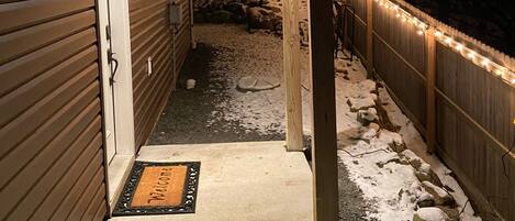 A covered outdoor area with a wooden deck, a snow-covered ground, and string lights.
