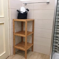 Un mobiletto contenitore in legno in un bagno, con un porta asciugamani sopra.