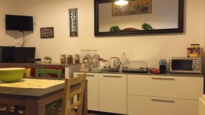A compact kitchen with a dining table, chairs, a microwave, a kettle, and various kitchen items. - Yooroom (Palermo)