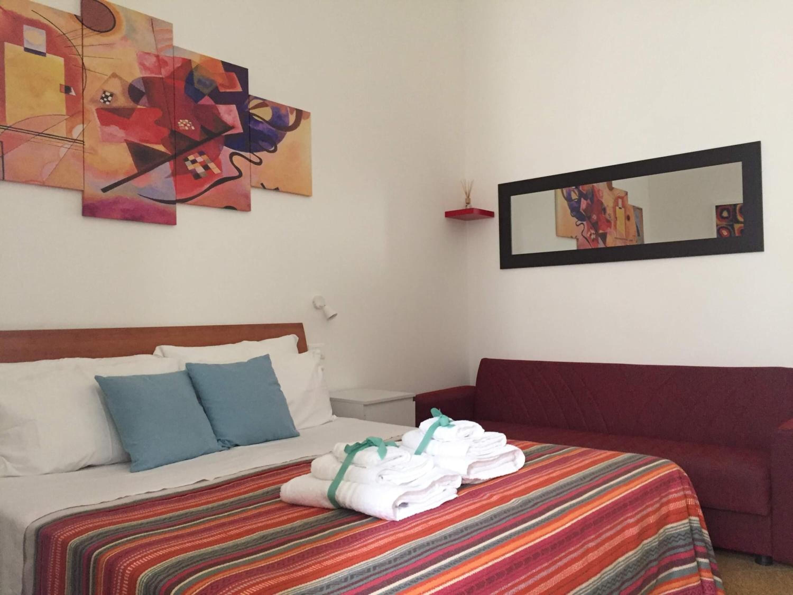 Una camera d'albergo con un letto, un divano rosso e dipinti astratti alle pareti.