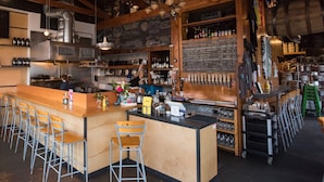 Un bar con una barra larga, varios taburetes y estantes llenos de botellas.