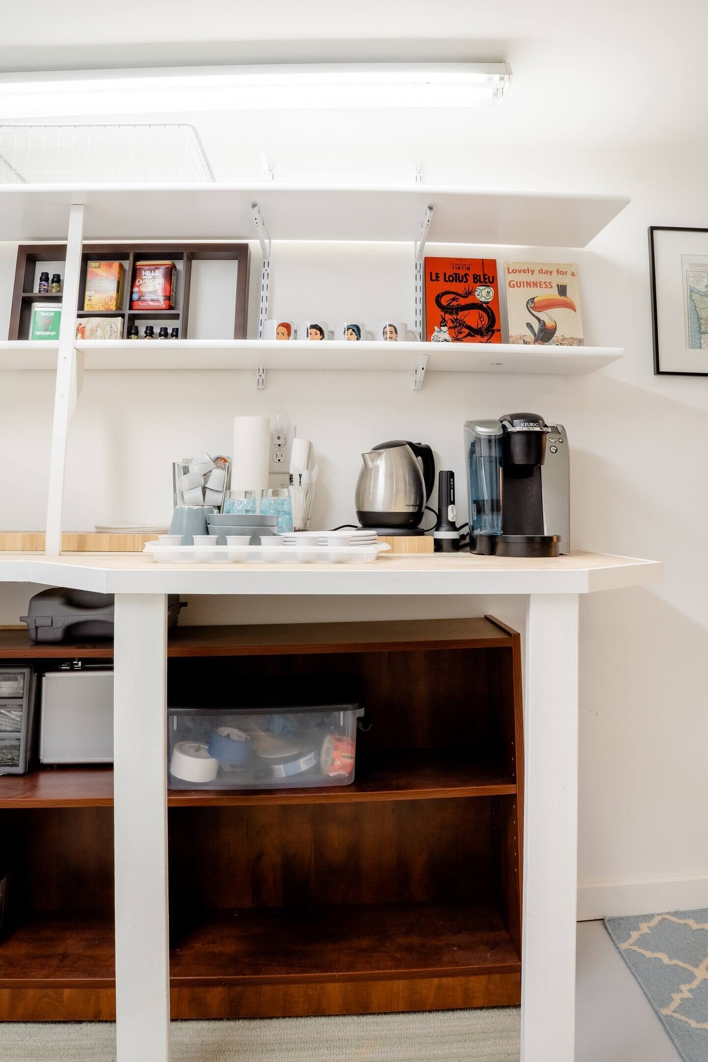 A kitchen area with a white countertop, coffee maker, kettle, and shelves with books and kitchen items.