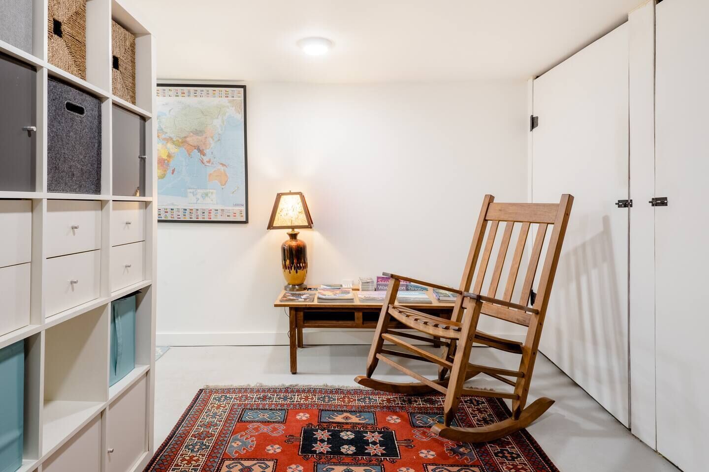 A room with a wooden rocking chair, a globe map on the wall, and a bookshelf with storage bins.