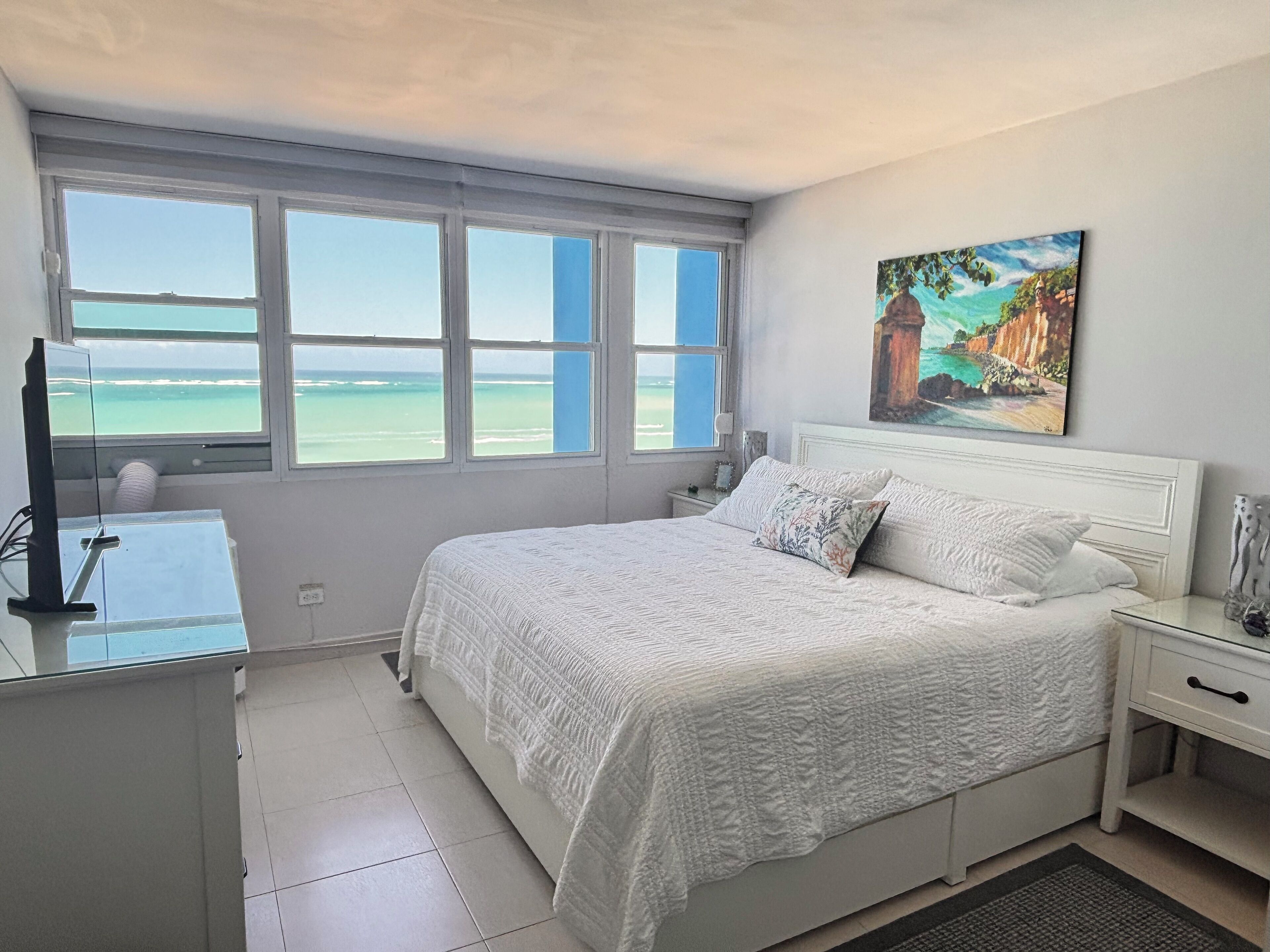 A bedroom with a large bed, a desk, and a window with a view of the ocean.