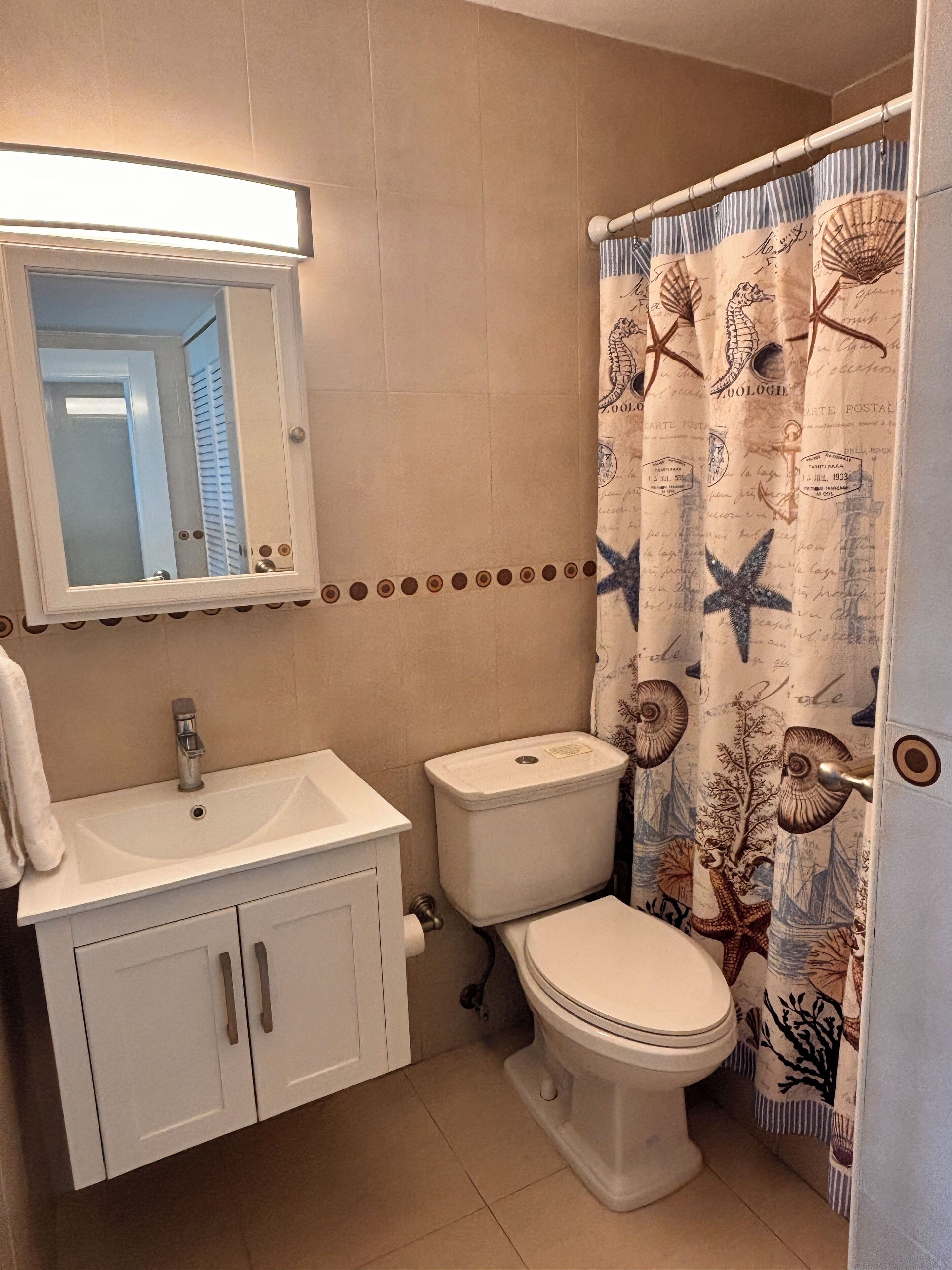 Een badkamer met een wit wastafel, toilet en een douchegordijn met nautische motieven.