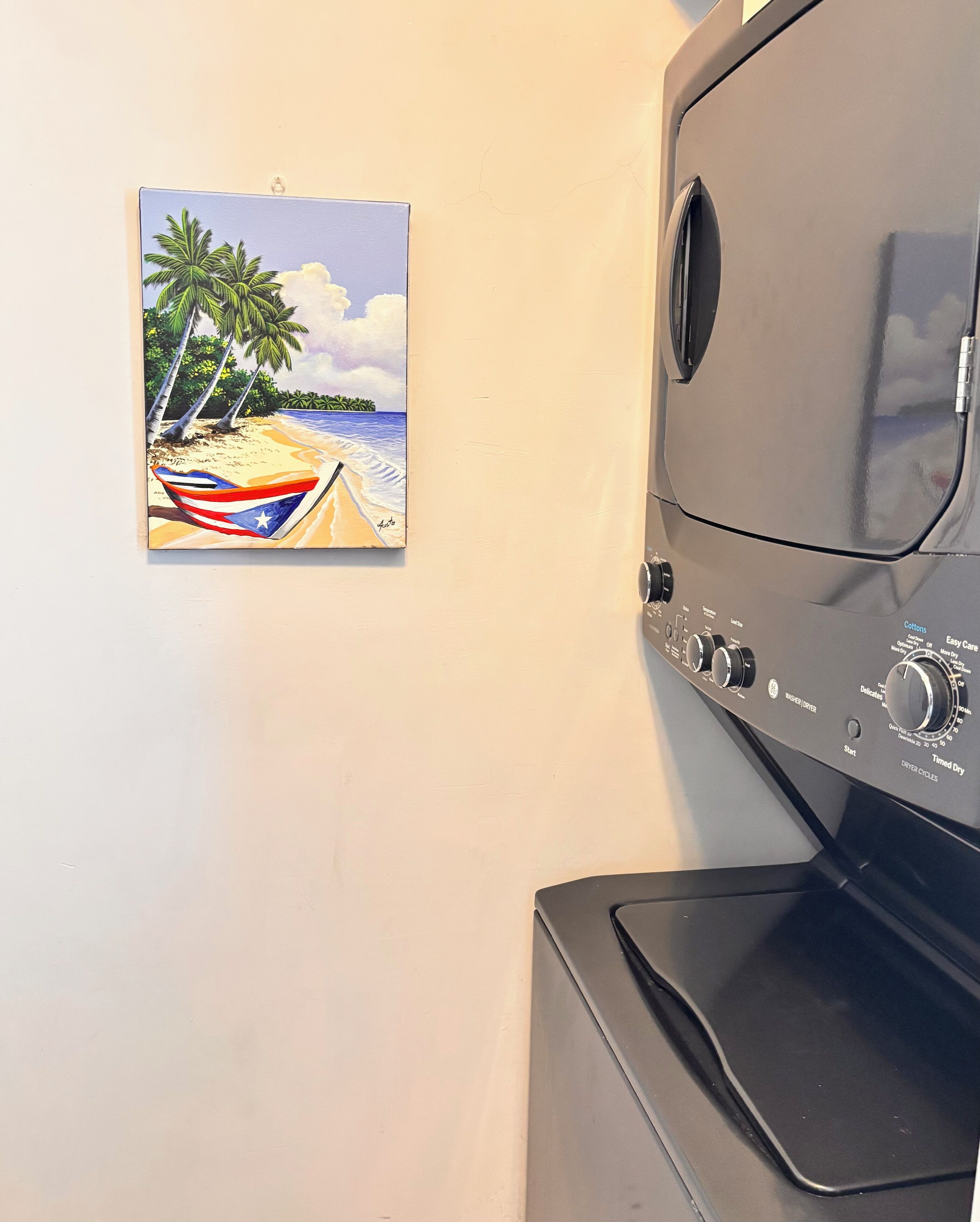 A wall-mounted painting of a beach scene with palm trees and a boat, next to a black appliance with control knobs and labels.