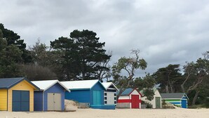 Filera de cabanes de platja amb una platja sorrenca i arbres al fons.