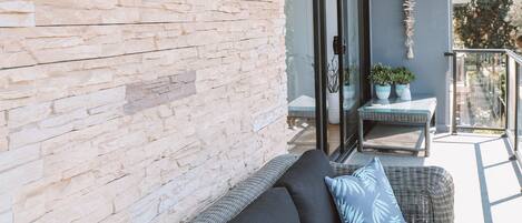 A balcony with a wicker sofa, a table with potted plants, and a stone wall.