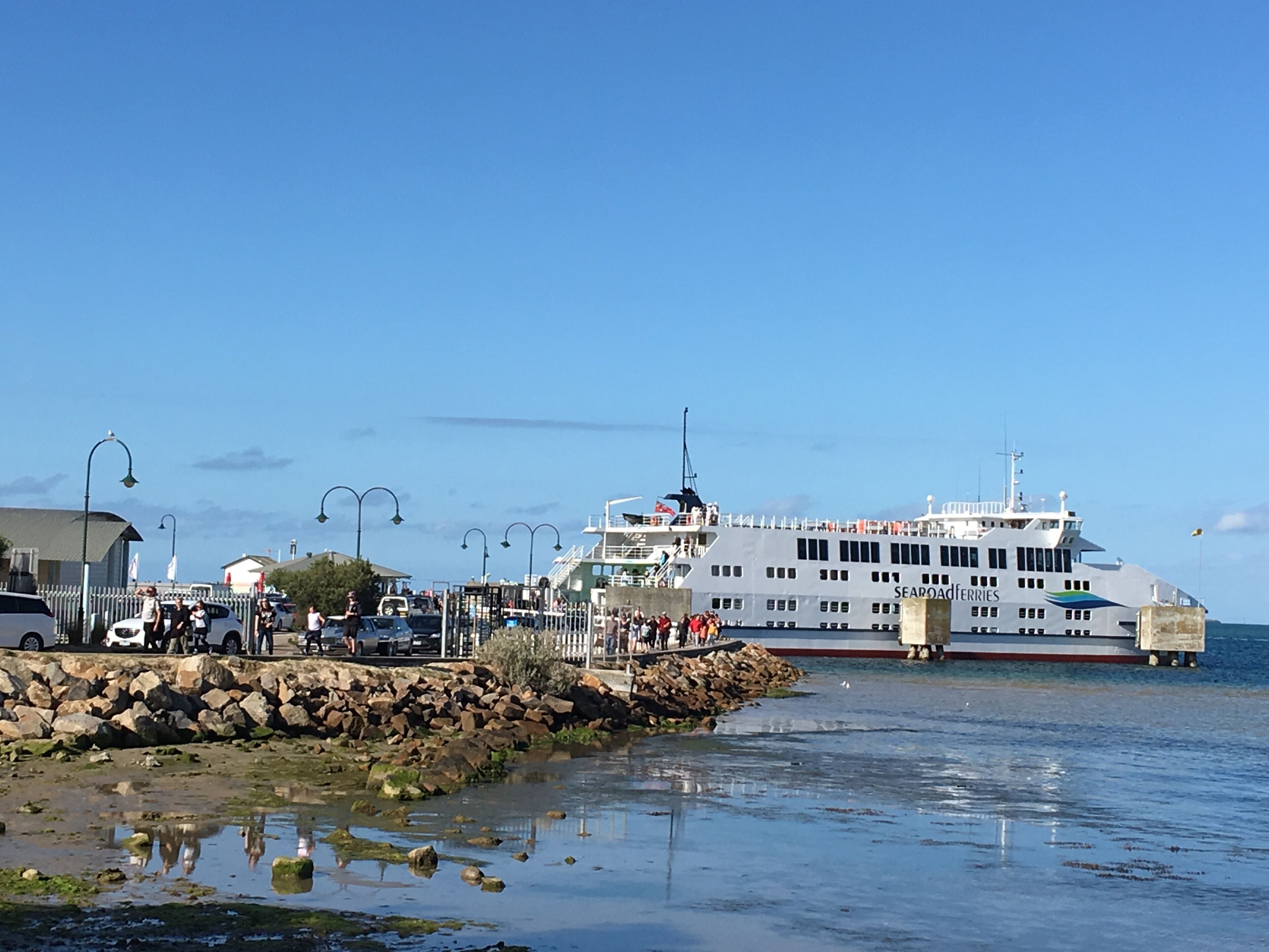 A ferry docked at a pier with a rocky shoreline and calm water.