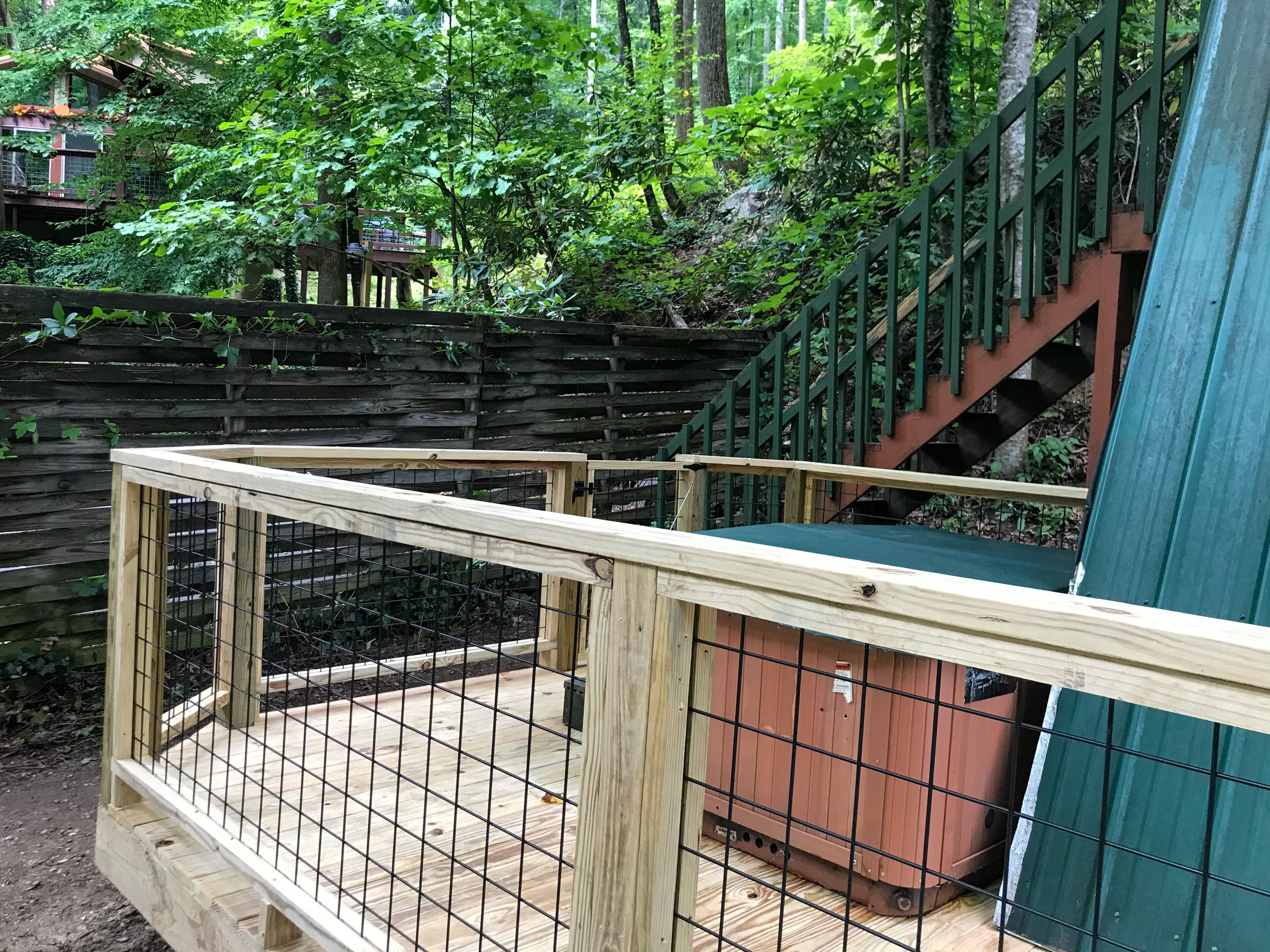 A wooden deck with a metal fence, surrounded by a wooden fence and greenery.