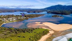 Vue aérienne d’une zone côtière comprenant une plage, un petit village et un lac entouré de collines.