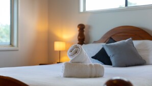 Un lit bien fait, avec une serviette enroulée, une tête de lit en bois et une table de chevet avec une lampe.