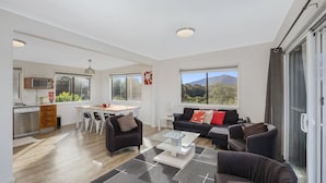 Une cuisine moderne avec un coin repas, un salon doté d’un canapé et d’une table basse, et de grandes fenêtres offrant une vue sur les montagnes.