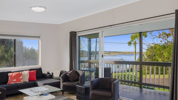 Un salon moderne doté d’une grande porte-fenêtre coulissante donnant sur un balcon avec vue sur un lac et la verdure environnante.