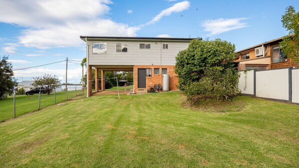 A two-story house with a covered patio, a fenced yard, and a small tree. - 8 Lakeview Drive - Water views (WALLAGA LAKE)