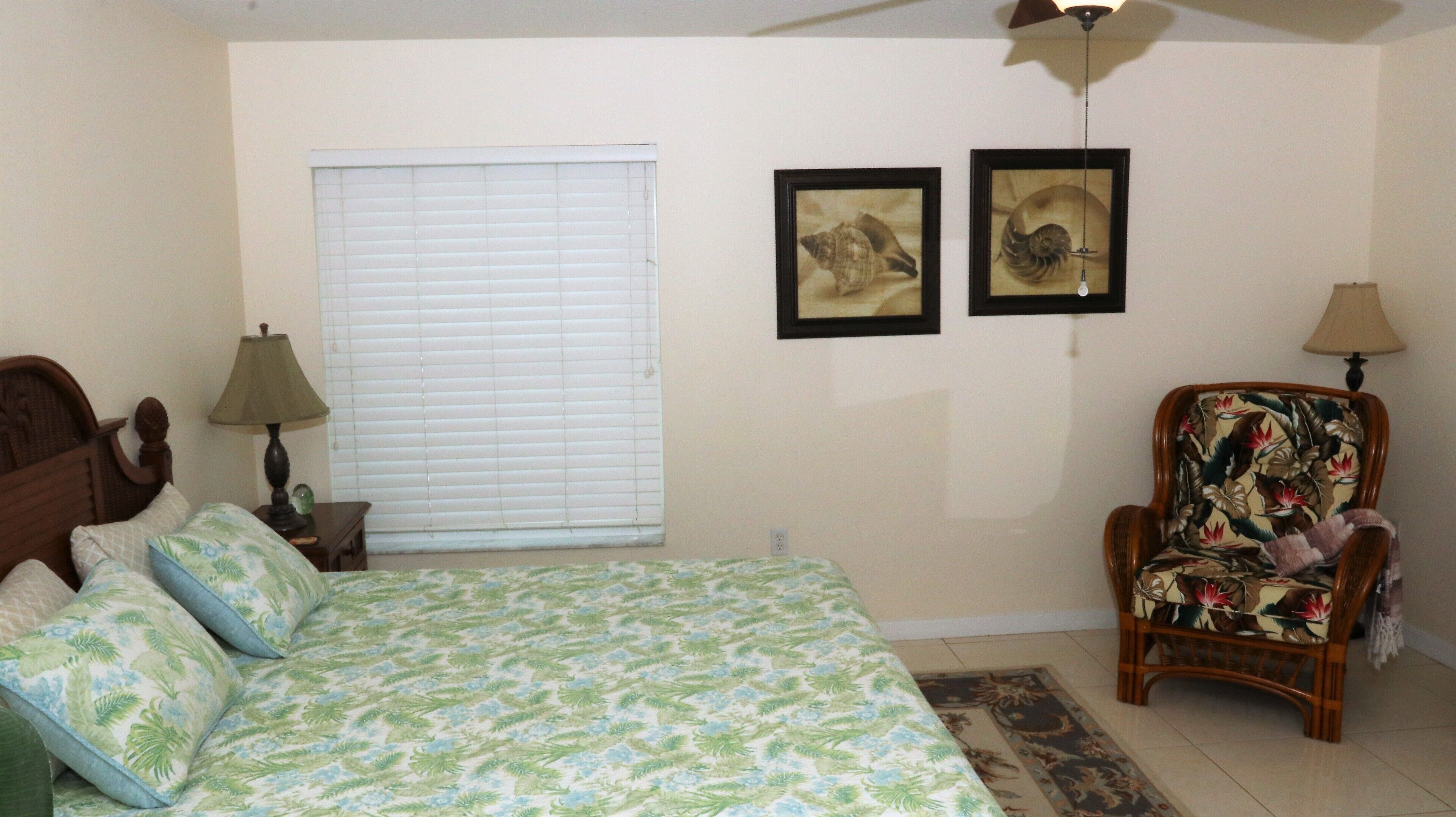 A bedroom with a bed, a chair, a window with blinds, and two framed pictures on the wall.