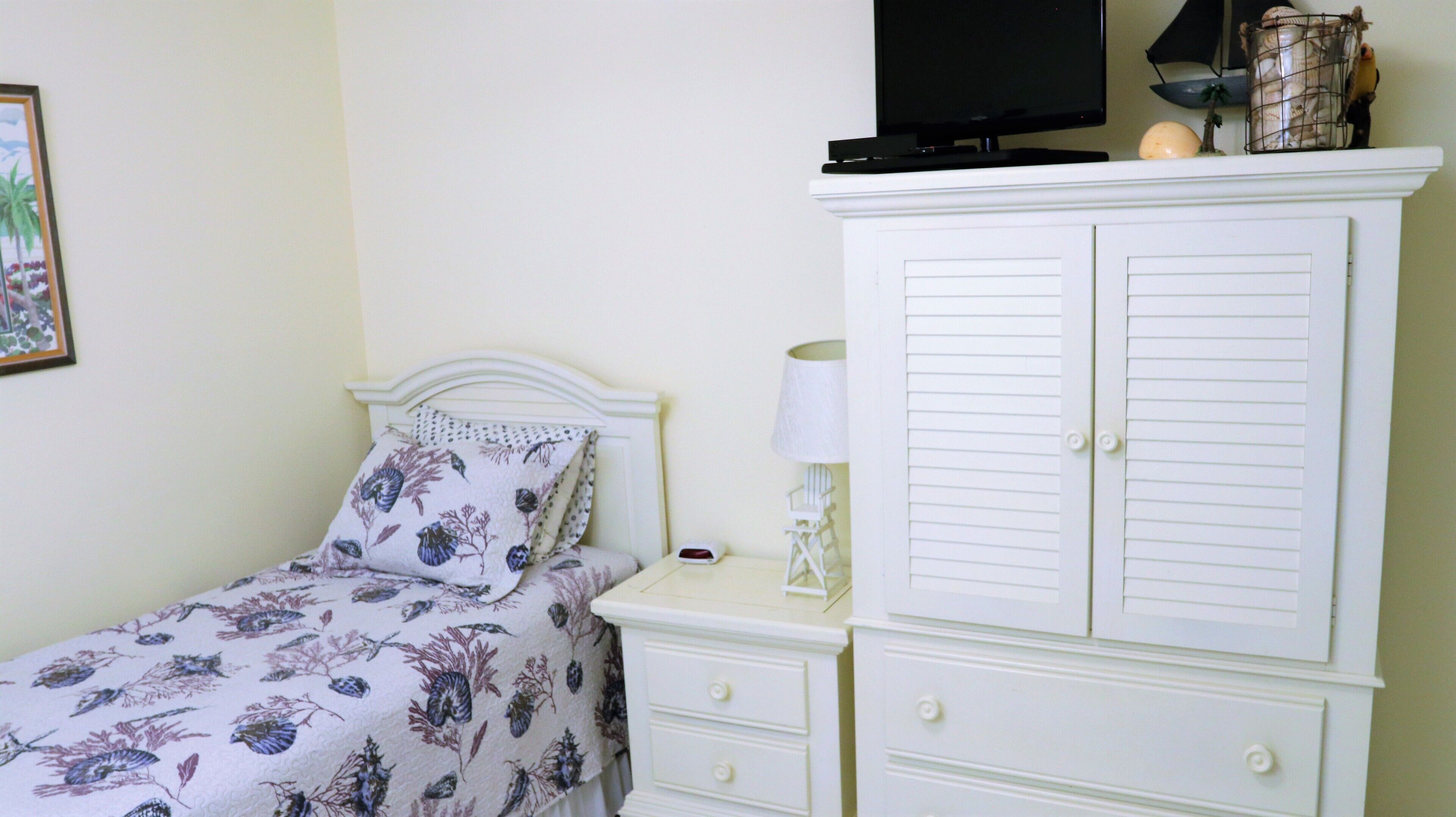 A bedroom with a bed, a nightstand, a lamp, a wardrobe, and a television on a stand.