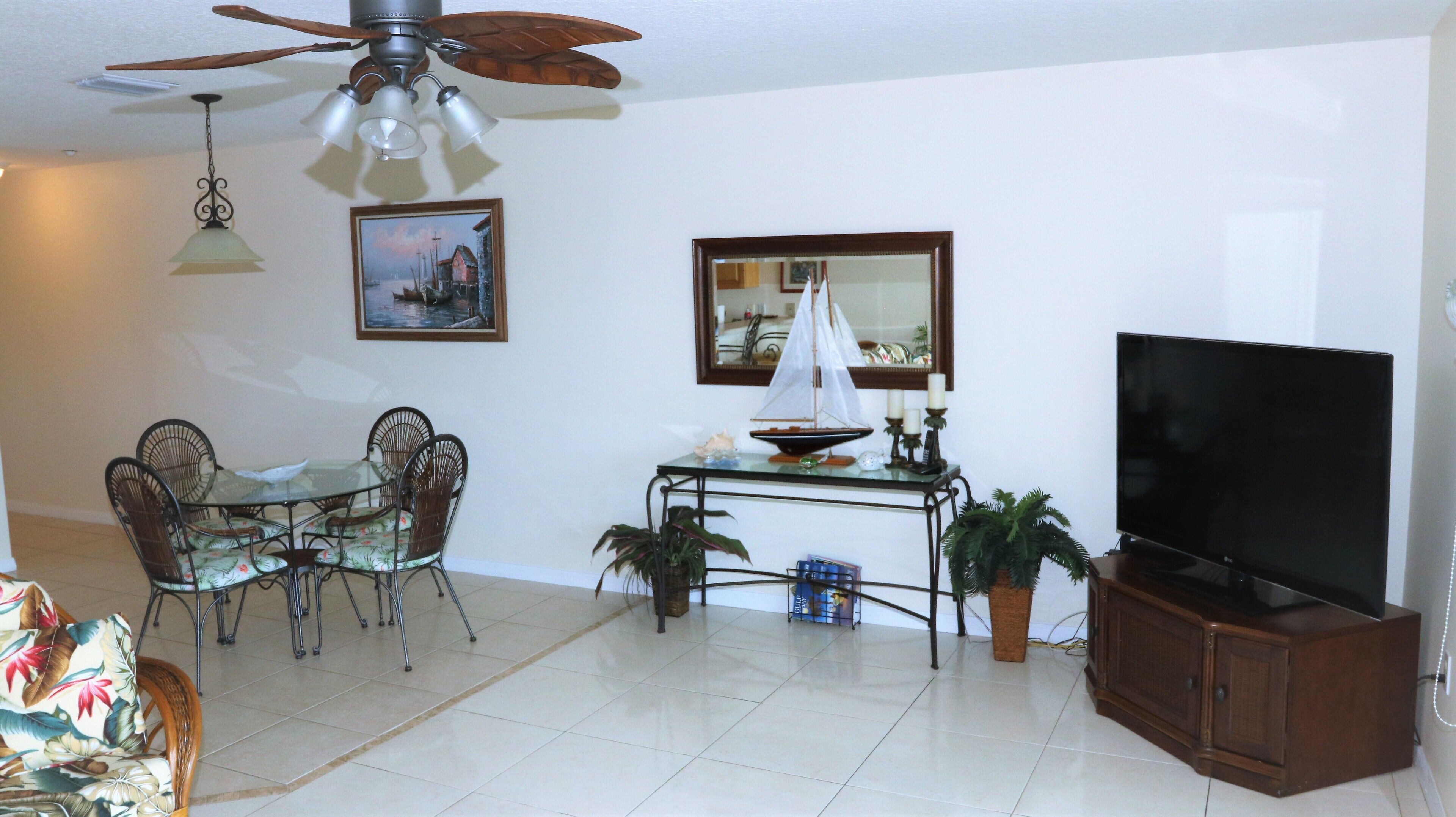 A living room with a dining table, chairs, a ceiling fan, a television, and a small sailboat model.