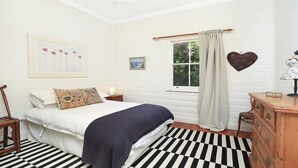 A bedroom with a bed, a dresser, a nightstand, a window with curtains, a wall-mounted picture, and a checkered floor.