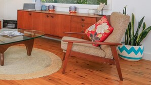A cozy living room with a wooden floor, a glass coffee table, a beige armchair with a floral pillow, a wooden cabinet, and a potted plant. - Poppy Cottage – delightful and pet-friendly cottage (Exeter)