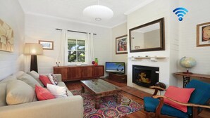 A living room with a sofa, armchair, TV, fireplace, and a globe on a side table. - Poppy Cottage – delightful and pet-friendly cottage (Exeter)