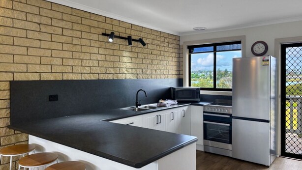 Una cocina moderna con pared de ladrillo, una isla grande, microondas, horno y refrigerador.