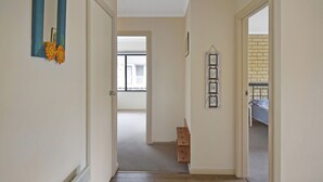 Un pasillo con una puerta que da a un balcón, un taburete de madera y un cuadro colgado en la pared.