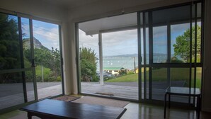 Quarto com uma grande porta de correr de vidro que dá para uma varanda com vista para a água e vegetação.